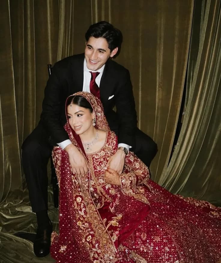 The couple seated together against a green velvet curtain